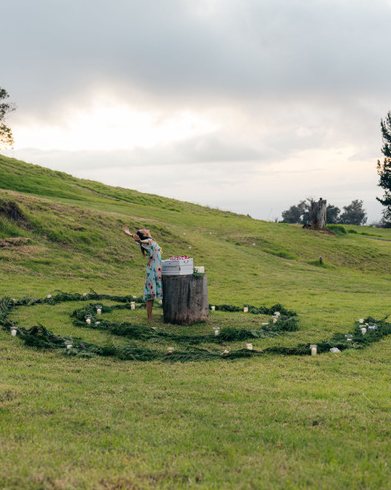 Ashana Sophia inside a spiral of greenery and candles on a green hillside under a moody sky